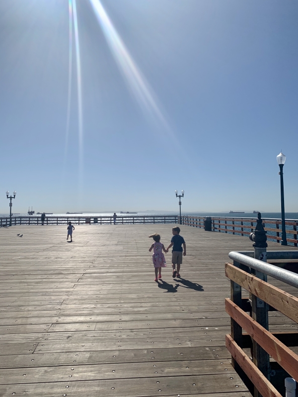 Two young children, holding, hands, happily running down the pier towards the ocean. 